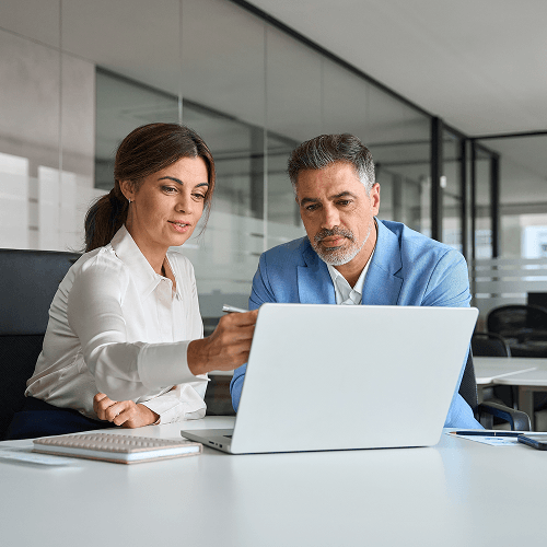 Dos ejecutivos revisan información juntos en una laptop dentro de una sala de juntas corporativa.