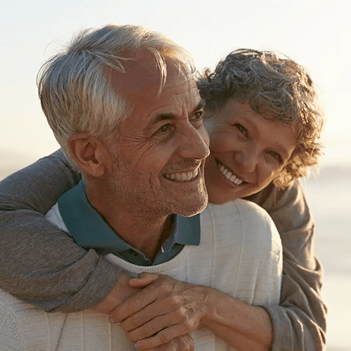 Pareja de adultos mayores sonriendo y abrazándose al aire libre con luz cálida de atardecer.