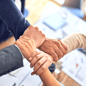 Cuatro personas entrelazan sus manos y muñecas formando un cuadrado, símbolo de unión y trabajo en equipo.